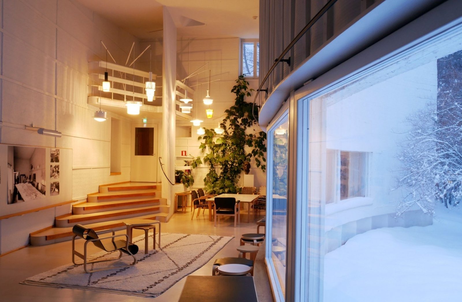 Korkeassa huoneessa on useita erilaisia tuoleja ja pöytiä, ja tilaa valaisee erilaisten valaisinten ryhmä. Oikealla on kaarevalla seinällä nauhamainen ikkuna, jonka kautta näkyy luminen talvikeli.. Kuvaaja: Jonas Malmberg Korkeassa huoneessa on useita erilaisia tuoleja ja pöytiä, ja tilaa valaisee erilaisten valaisinten ryhmä. Oikealla on kaarevalla seinällä nauhamainen ikkuna, jonka kautta näkyy luminen talvikeli.. Kuvaaja: Jonas Malmberg