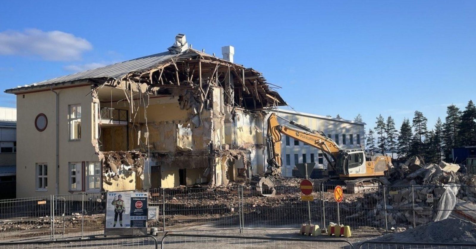 Puoliksi purettu 1930-luvun tiilirakenteinen koulu, jonka vieressä on purkuun käytetty kaivinkone sekä kasa purkujätettä.
