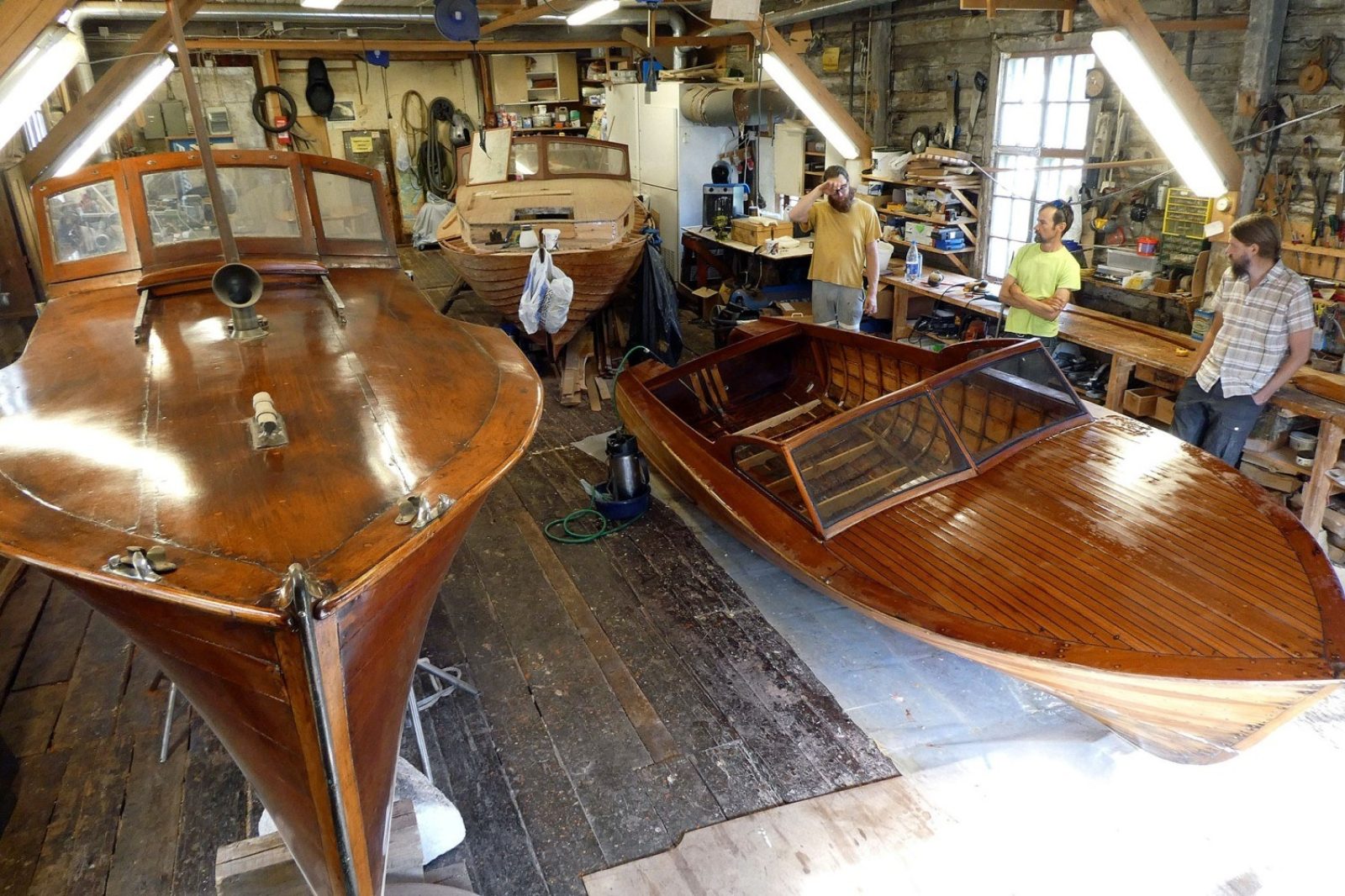 Kolme puuvenettä hallitilassa. Oikealla kolme miestä juttelemassa.