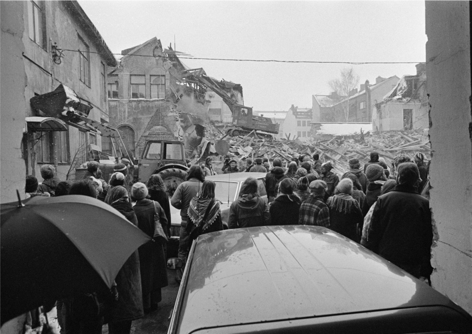 Väkijoukko kerääntyneenä purkutyömaalle, jossa kaivinkoneet hajottavat 1890-luvun kivirakennusta.