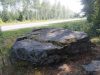 Laakea kivenlohkare, jossa kaiverruksia. Taustalla tie ja sen takana metsää.