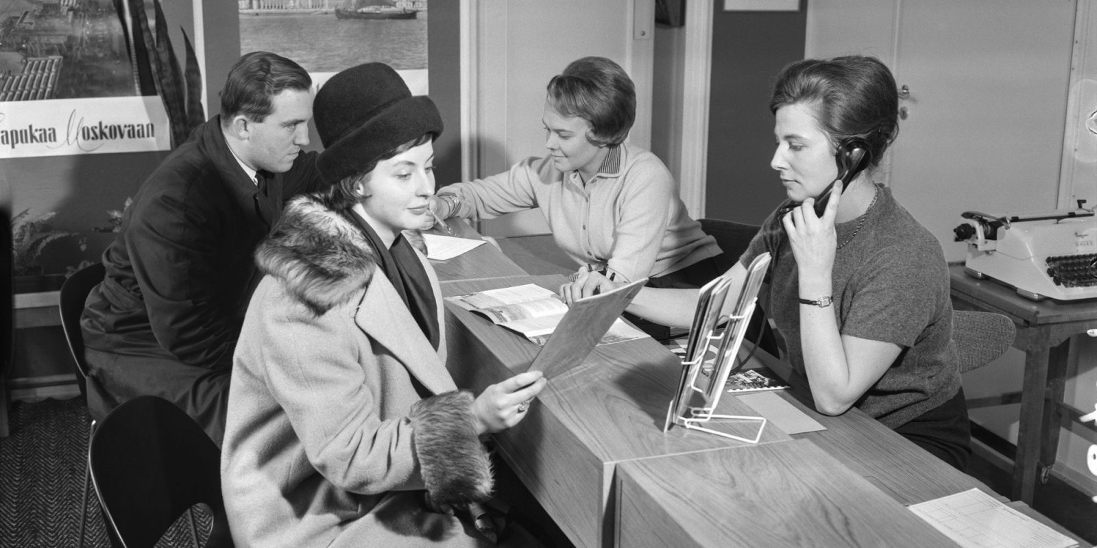 Kaksi asiakasta ja kaksi asiakaspalvelijaa mustavalkoisessa valokuvassa vuodelta 1961. Kaksi asiakasta ja kaksi asiakaspalvelijaa mustavalkoisessa valokuvassa vuodelta 1961.