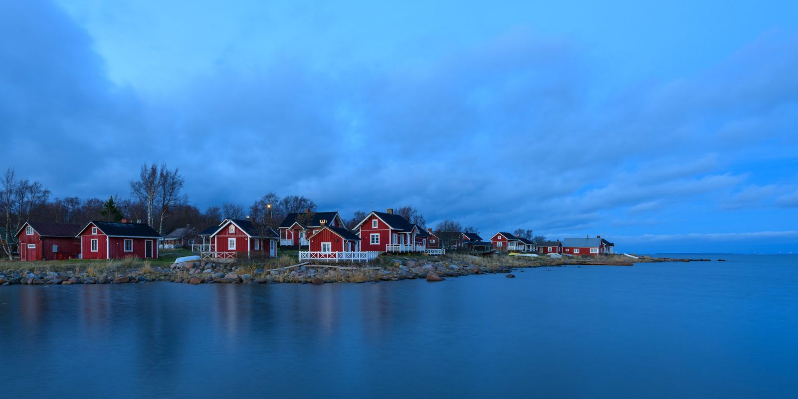 Iltahämärässä otetussa kuvassa kallioinen luoto, jolla useita punaseinäisiä puutaloja. Etualalla tyyni meri.. Kuvaaja: Teuvo Salmenjoki Iltahämärässä otetussa kuvassa kallioinen luoto, jolla useita punaseinäisiä puutaloja. Etualalla tyyni meri.. Kuvaaja: Teuvo Salmenjoki