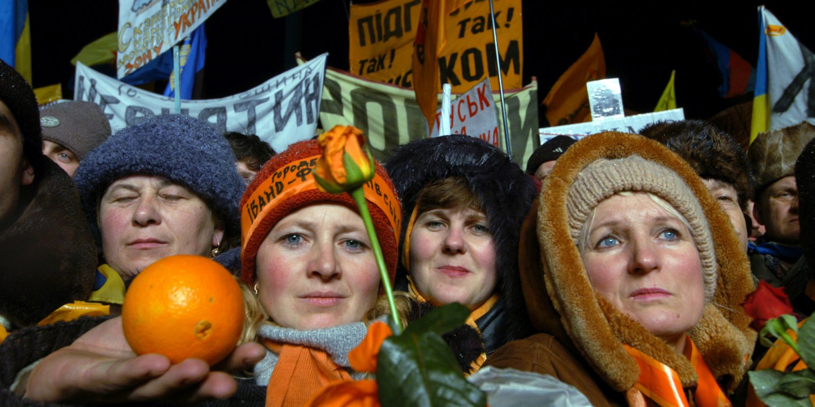 Neljä naista talvipäähineissä. Yhdellä on kädessään appelsiini. Taustalla näkyy mielenosoittajien kylttejä.. Kuvaaja: Hannu Lindroos / Journalistinen kuva-arkisto JOKA / Museovirasto. Objektinumero: SK10271_70 Neljä naista talvipäähineissä. Yhdellä on kädessään appelsiini. Taustalla näkyy mielenosoittajien kylttejä.. Kuvaaja: Hannu Lindroos / Journalistinen kuva-arkisto JOKA / Museovirasto. Objektinumero: SK10271_70
