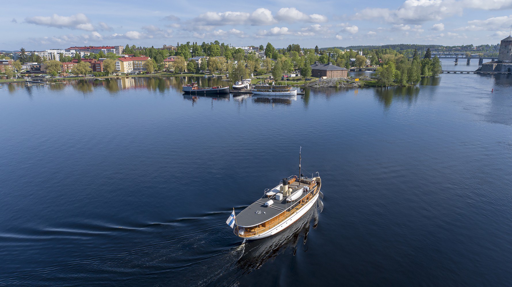 Alus ajaa järvellä kohti taustalla näkyvää Savonlinnan kaupunkia ja Olavinlinnaa.