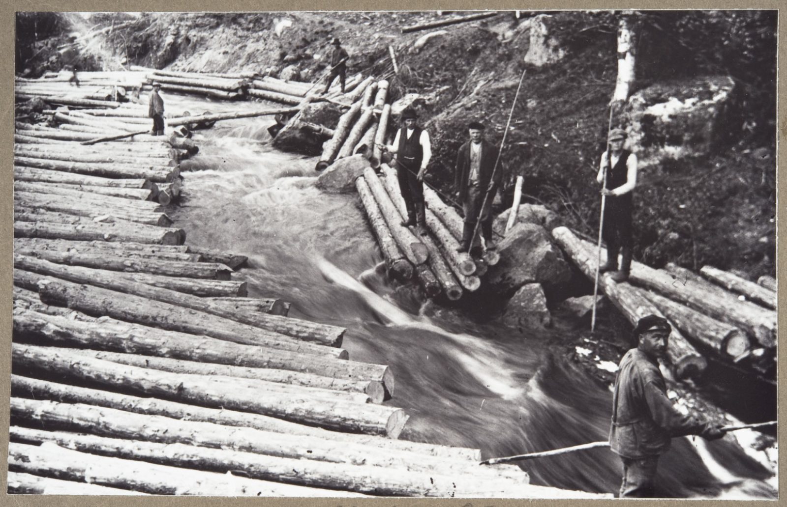 Mustavalkovalokuva tukinuitosta Juvan Koikkalanjoella 1920-luvulla, jossa miehiä uittohommissa virtaavan veden keskellä. Mustavalkovalokuva tukinuitosta Juvan Koikkalanjoella 1920-luvulla, jossa miehiä uittohommissa virtaavan veden keskellä.