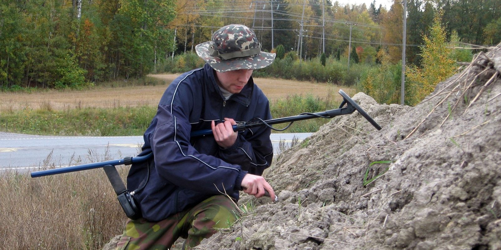 Mies korkean multakasan rinteellä. Hänellä on metallinilmaisin kainalossaan.