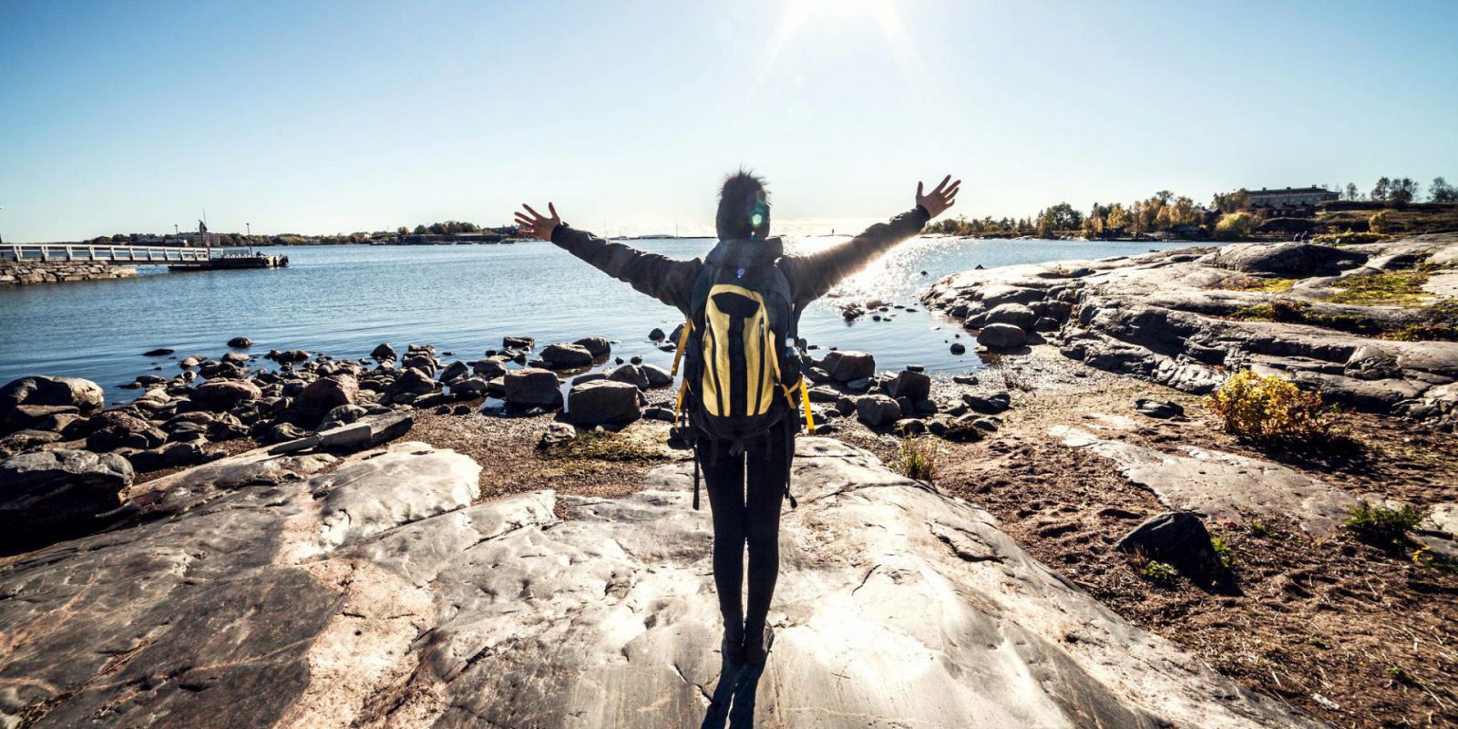 Henkilö kivikkoisella merenrannalla auringonpaisteessa kädet levitettyinä.. Kuvaaja: iStock / Marco Piunti Henkilö kivikkoisella merenrannalla auringonpaisteessa kädet levitettyinä.. Kuvaaja: iStock / Marco Piunti