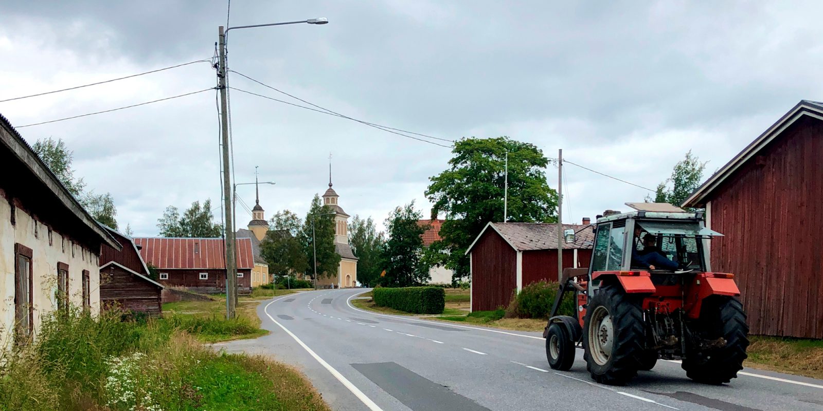 Purmon keskusta Pohjanmaalla. Traktroi ajaa maalaistietä, jonka varrella on puurakennuksia. Kauempana siintää kirkko.. Kuvaaja: Tapio Heikkilä, SYKE Purmon keskusta Pohjanmaalla. Traktroi ajaa maalaistietä, jonka varrella on puurakennuksia. Kauempana siintää kirkko.. Kuvaaja: Tapio Heikkilä, SYKE
